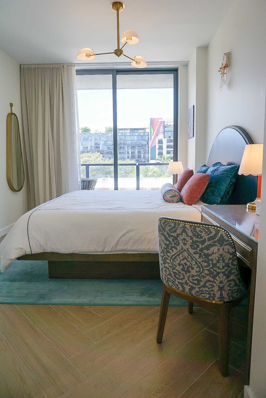 Full bedroom — king bed, brass chandelier, floor-to-ceiling windows