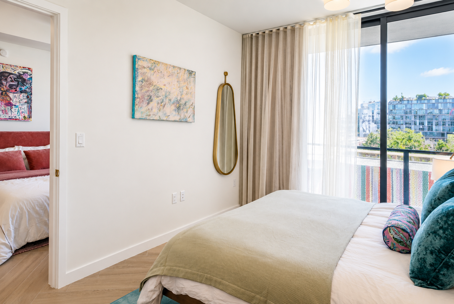 Bedroom looking toward balcony — gold oval mirror, herringbone floors